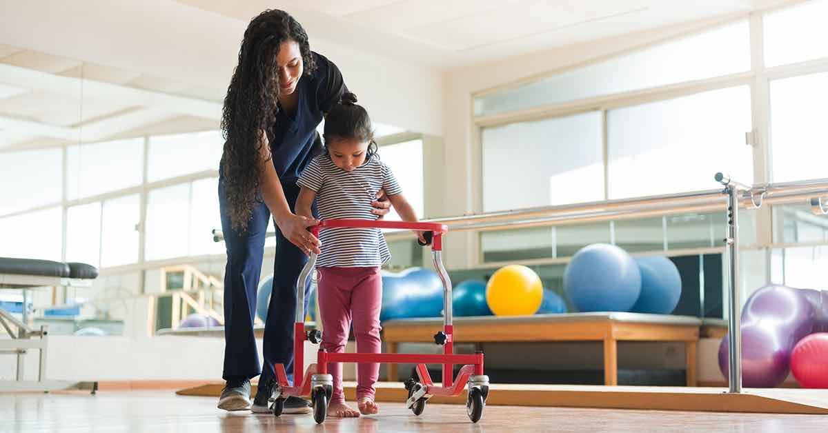 A physical therapist helping a child practice walking with an adaptive walker